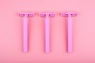 Pembe arka planda tıraş olmak için üç plastik jiletin üst görünümü