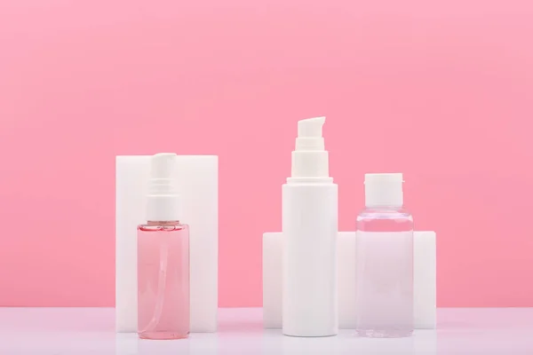 Pembe arka planda düzenli cilt bakımı için güzellik ürünleri içeren kozmetik şişeleri.. 