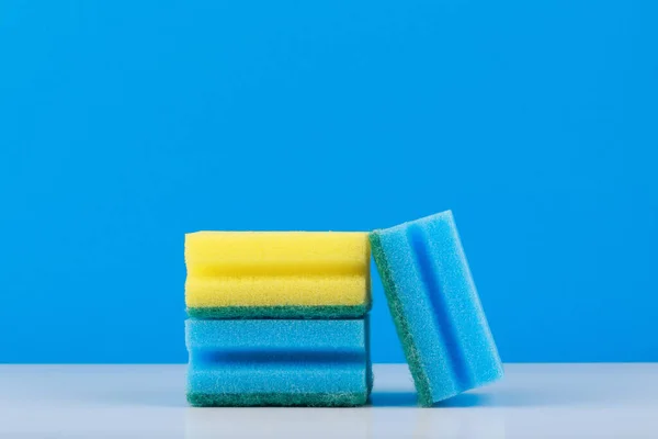Éponge bleue et jaune pour le nettoyage et le lavage des plats sur table blanche sur fond bleu avec espace de copie — Photo