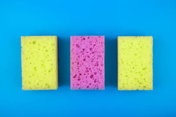 Esponjas amarillas y moradas para la limpieza de la casa y el lavado de platos sobre fondo azul — Foto de Stock