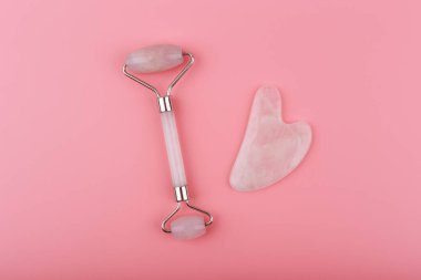 Pembe arka planda pembe kuvarstan yapılmış yeşim taşlı ve kalp şeklinde masaj aleti. Guasha masaj konsepti