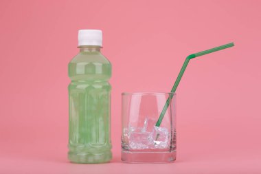 Yeşil içecek, şeffaf şişede meyveler ve pembe arka planda buzla dolu bardaklar.