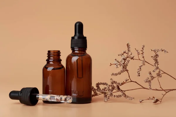 Selective focus, two dark transparent glass bottles with skin serum or oil for manicure on beige background decorated with dry flower — Stock Photo, Image