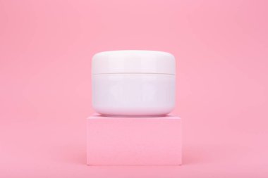 Pembe kürsüde beyaz krema kavanozu parlak pembe arka planda