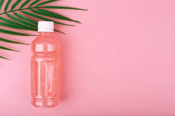 Flat lay with pink drink in transparent plastic bottle against pink background with palm leaf and copy space — Stock Photo, Image