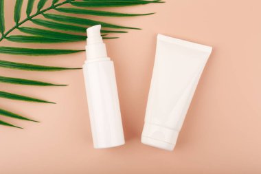 Krem, losyon ya da günlük cilt bakımı için palmiye yapraklı pastel bej arka planda kozmetik şişeleri ile yaratıcı düz uzanma
