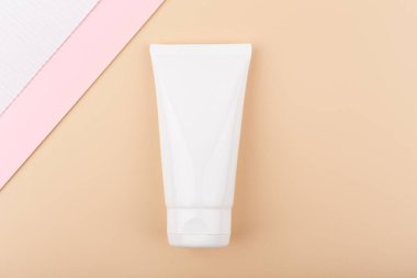 Yüzü veya el kremi ya da kremi ile beyaz ve pembe kağıtlarla dekore edilmiş parlak pastel bej arka planda krem sürmüş yaratıcı düz bir yatak. Cilt bakımı için güzellik ürünleri kavramı