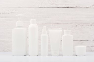 Beyaz ahşap arka planda yüz ve vücut bakımı için beyaz markasız kozmetik şişeler. Organik, doğal, çevre dostu kozmetik ürünleri ve güzellik ürünleri kavramı