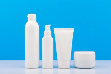 Günlük cilt bakımı için beyaz markasız kozmetik şişeler beyaz masada mavi arka planda. İnsan ve hijyen için cilt bakım ürünleri kavramı