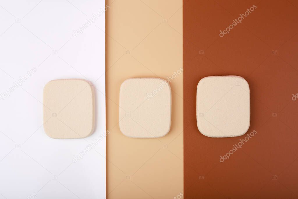 Creative flat lay with three square shaped make up sponges on white, beige and brown background. Concept of make up for all skin tones from light to dark