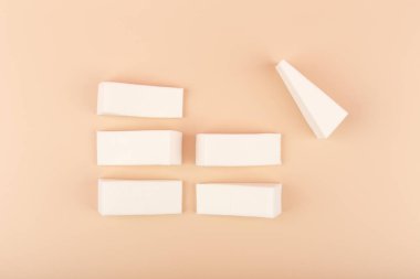 Parlak pastel bej arka planda izole edilmiş beyaz üçgen şekilli makyaj süngerleri ile yaratıcı düz yatıyordu. Güzellik karıştırıcıları, profesyonel makyaj ve görünüm için sünger ve araçlar