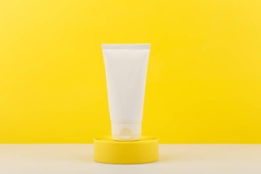 Sarı kürsüde beyaz tüpte yüz ya da eller krem sürerken sarı zemin üzerinde kopya alanı var.