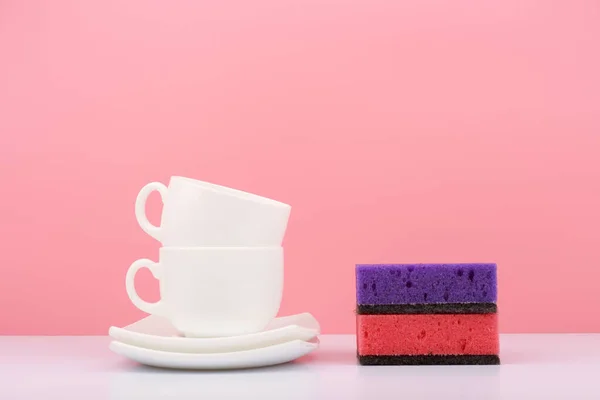 Dishwashing concept. Plates, cups and cleaning sponges against bright pink background — Fotografia de Stock