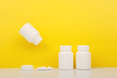 Creative layout with vitamins bottles on white table against yellow background