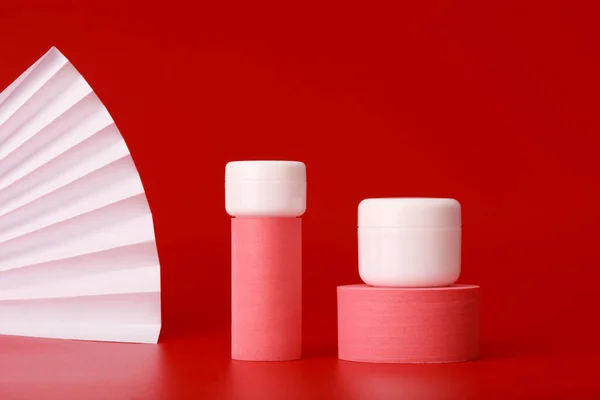 Două borcane de cremă pe forme geometrice roz pentru prezentarea produsului pe fundal roșu cu ondulator — Fotografie, imagine de stoc