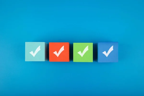 Dört renkli oyuncak bloğu ve mavi arka planda kontrol işaretleri olan yaratıcı bir daire. Sorgulama kavramı, kontrol listesi, yapılacaklar listesi, planlama veya iş planları