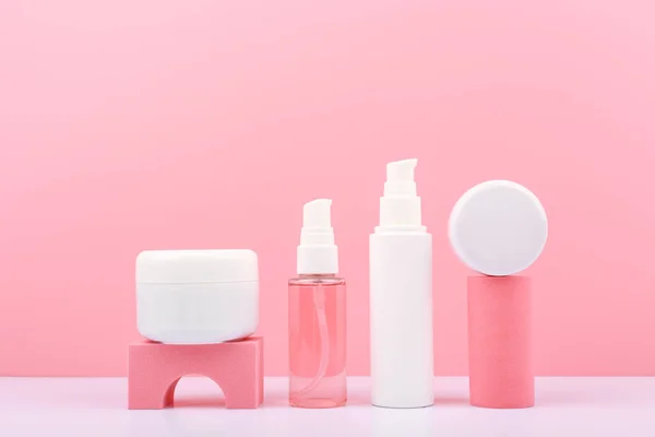 Pembe renklerde moda bir kompozisyon. Kozmetik şişeler, geometrik malzemeler, pembe arka plan. Parlayan, genç görünümlü ciltler için organik kozmetik kavramı