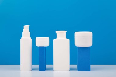 Günlük cilt bakımı için beyaz markasız kozmetik şişeler. Parlak mavi arka planda ürün sunumu için geometrik aksesuarlar. Hijyen anlayışı, insanın cilt bakımı veya akne tedavisi