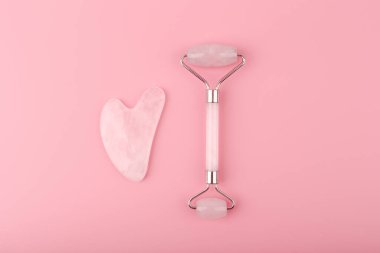 Pembe arka planda pembe kuvarstan yapılmış yeşil silindir ve kalp şeklinde guasha kazıyıcı. Kendini tedavi etme kavramı ve cilt gerdirme ve tonlama için yüz masajı.