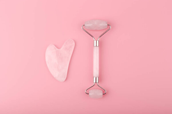 Нефритовые ролики и сердце форме гуаши скребок массажер из розового кварца на розовом фоне. Концепция самолечения и массажа гуаши для поднятия и тонизации кожи