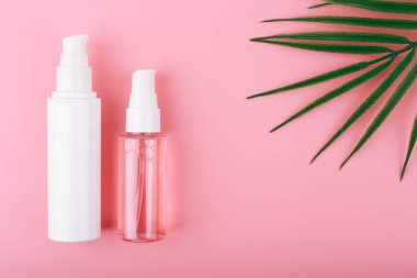 Yüz temizleme, cilt temizleme ve nemlendirme için fotokopi alanı ve palmiye yaprağı ile pembe arka plana karşı bir takım kozmetik şişeler. Moda modern daire günlük kullanım için güzellik ürünleri seti ile yatıyordu 