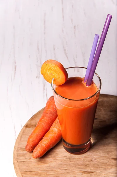 Mor tüpler ve havuç bir ahşap masa üstüne uzun bir bardak taze havuç suyu