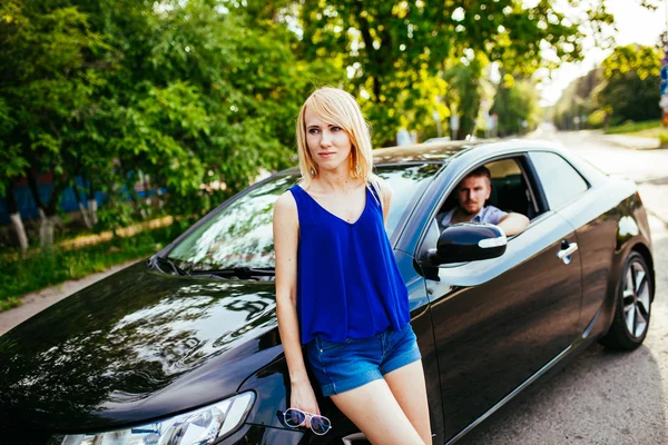 Girl standing near the car. A man sitting in a car.