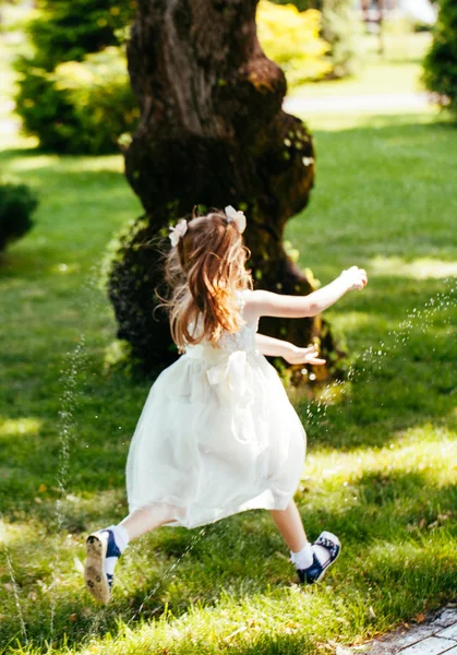 Heureuse petite fille courir à travers la pulvérisation d'eau dans le parc — Photo