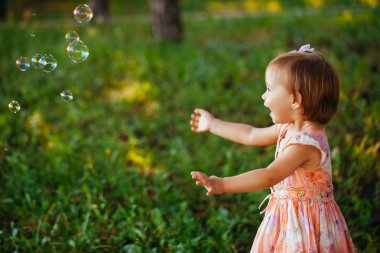 Sevimli küçük bir kız parkta sabun köpüğü ile oynarken.