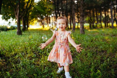 Sevimli küçük bir kız parkta sabun köpüğü ile oynarken.