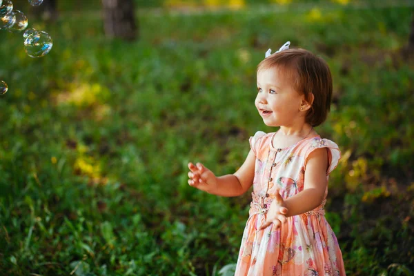 Una bambina carina che gioca con le bolle di sapone nel parco . — Foto Stock