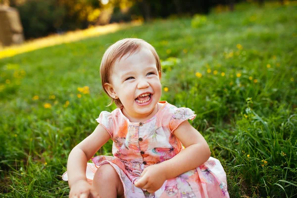 Liten flicka sitter på gräset. — Stockfoto