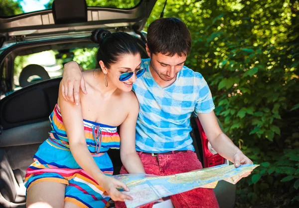 Young travelers looking at map while sitting in trunk of a car