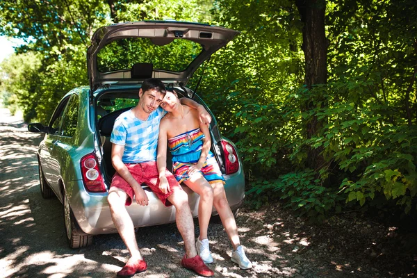 Young travelers looking at map while sitting in trunk of a car — Stock Photo, Image