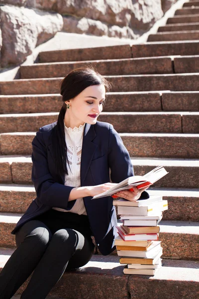 美丽的女学生是坐在楼梯上，读一本书 — 图库照片