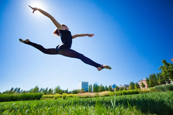 Lächelnde junge Turnerin springt in Split und schwebt über dem — Stockfoto