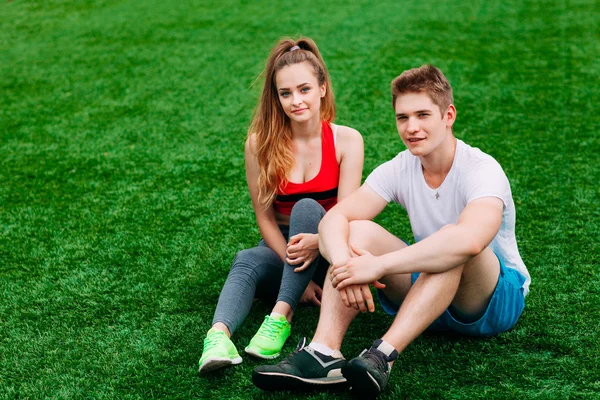 Junges sportliches Paar sitzt auf dem Rasen — Stockfoto