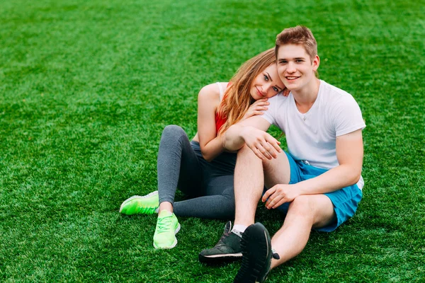 Çimenlerin üzerinde oturan genç atletik Çift