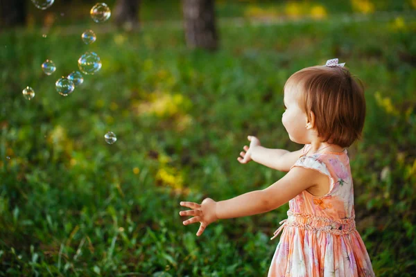 A cute little girl playing with soap bubbles in the park. — Stock Photo, Image
