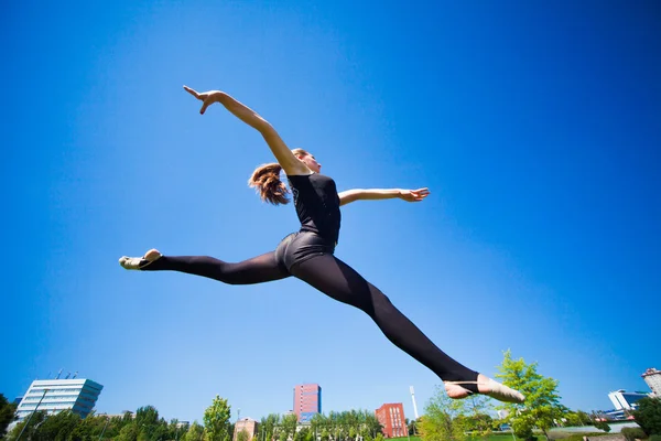 Sorridente giovane ginnasta sta saltando in split e galleggiante sopra il — Foto Stock
