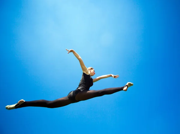 Smiling young gymnast is jumping in split and floating above the