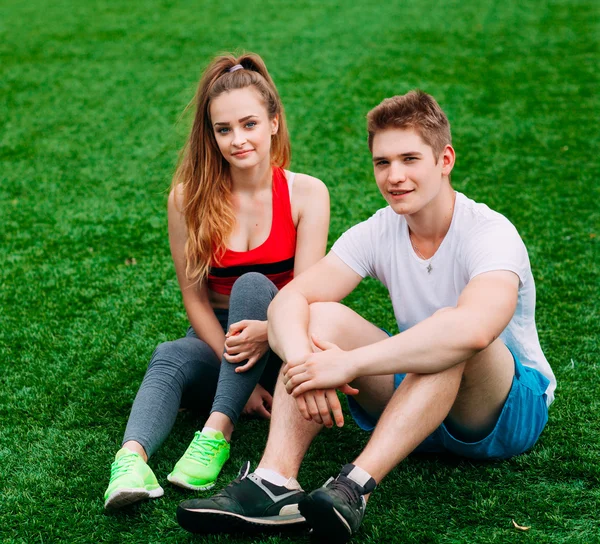 Junges sportliches Paar sitzt auf dem Rasen — Stockfoto