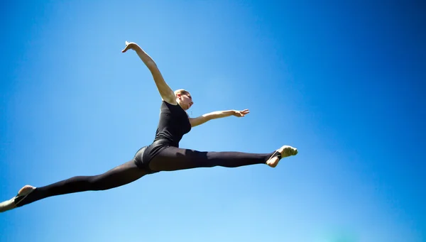 Smiling young gymnast is jumping in split and floating above the — Stock Photo, Image