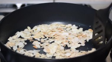 Metal bir tavada, tavada kızartılmış badem fıstığı karıştıran kadın eli..