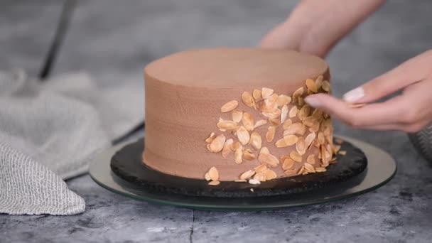 Kvinnlig konditor förbereder en tårta och dekorerar den med mandelflingor. — Stockvideo