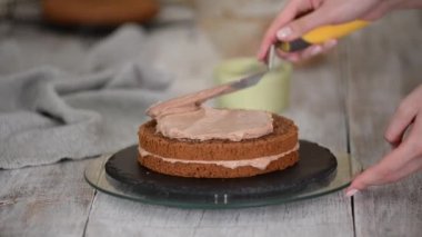Spatulalı bir kız kremayı çikolatalı süngerli pastaya sürüyor.