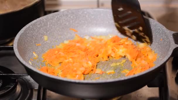 Mujer freír zanahorias con cebolla en una sartén en la cocina. — Vídeos de Stock