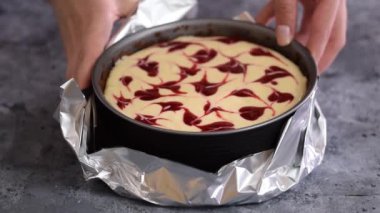 Mutfakta çilek soslu cheesecake hazırlayan kadın. İlkbahar tavasının etrafına alüminyum folyo sarılıyor.
