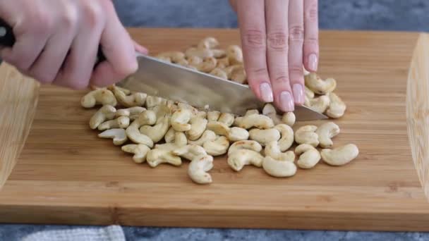 Close up: Womans hands with knife cut cashew nuts on a cutting board in a kitchen. — стоковое видео