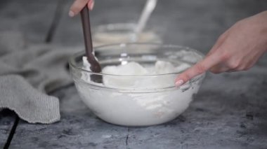 Bir kadının elindeki silikon spatula, kaju fıstığı, şeker ve un karışımını çırpılmış yumurta beyazının içine dikkatlice koyar. Kiş keki pişirmek için cam bir kasede kalın köpük.